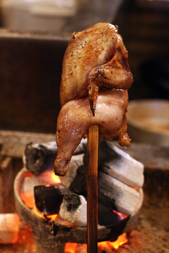 炭火でじっくり焼かれるがぶり鶏の半身。外は香ばしく中はふっくら仕上がる工程。